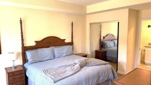 Un dormitorio con cama con dosel, una mesita de noche, un espejo y una puerta que da a un baño.