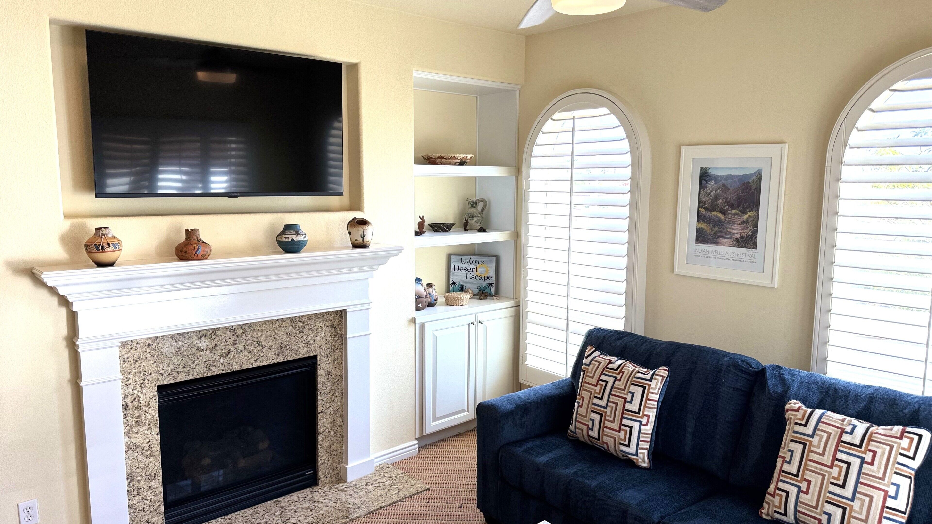 A living room with a fireplace, television, and decorative items on shelves.