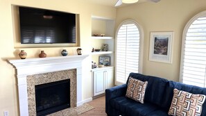 A living room with a fireplace, television, and decorative items on shelves. - Walking distance from the World Famous, Indian Wells Tennis Gardens (La Quinta)