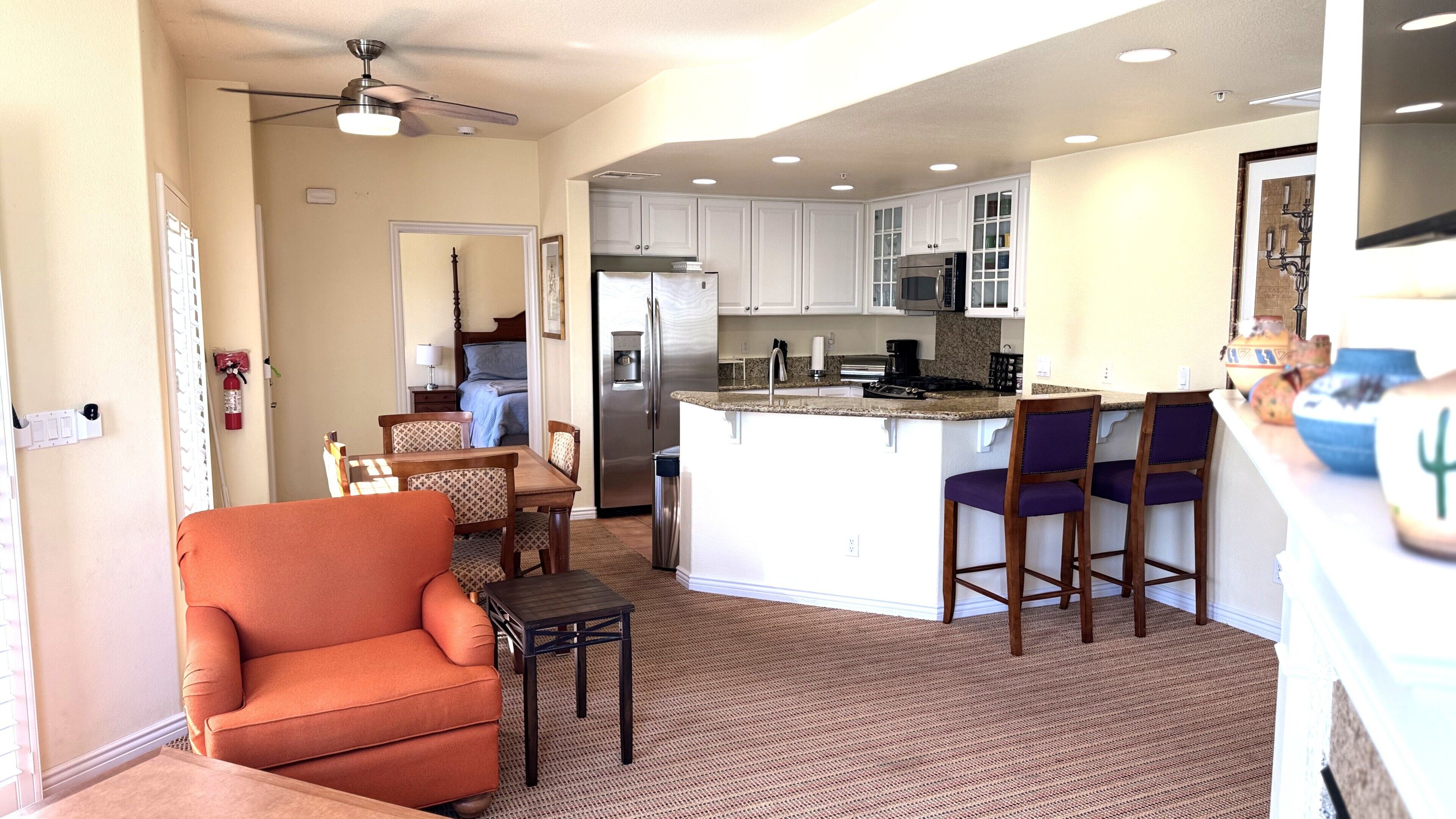 A compact kitchen with white cabinets, a central island with bar seating, and a dining area with a sofa and chairs.