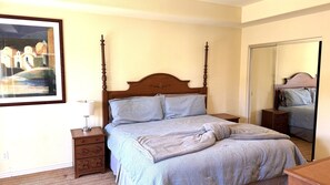 A bedroom with a four-poster bed, a bedside table with a lamp, a dresser, and a large mirror. - Walking distance from the World Famous, Indian Wells Tennis Gardens (La Quinta)