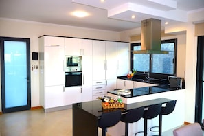 A modern kitchen with white cabinetry, a black countertop, and a stainless steel range hood. - Sunset Villa Madeira (Ribeira Brava)