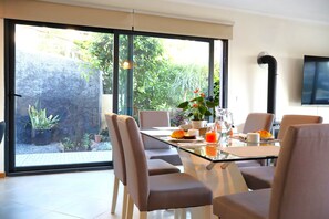 A modern dining area with a glass table, cushioned chairs, and a view of a garden through large windows. - Sunset Villa Madeira (Ribeira Brava)