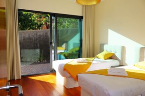 A hotel room with two beds, a sliding glass door leading to a balcony, and a view of greenery outside. - Sunset Villa Madeira (Ribeira Brava)