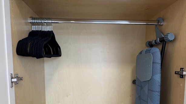 A compact room with a bed, a small shelf, and a hanging rack.