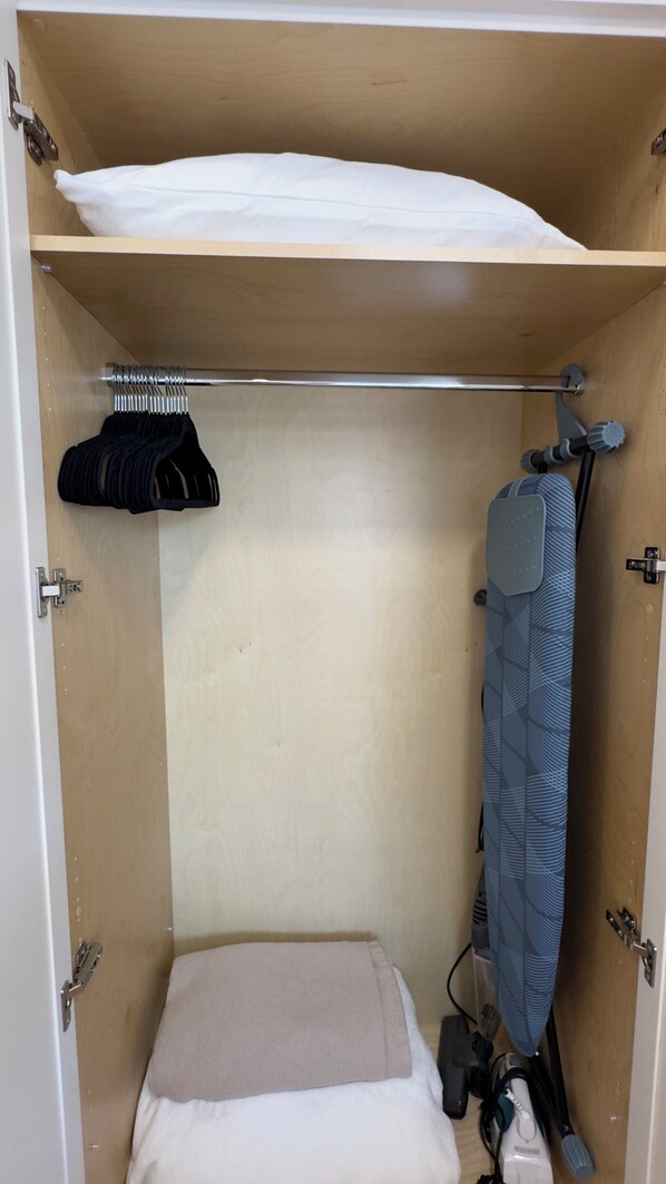 A compact room with a bed, a small shelf, and a hanging rack.