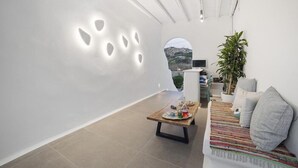Um interior moderno com uma parede branca, uma mesa de madeira com uma bandeja de objetos, um sofá com almofadas e um vaso de planta.