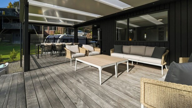 Une terrasse extérieure avec une plateforme en bois, un canapé blanc et des fauteuils en osier.