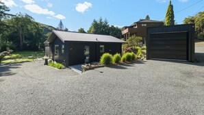 Un petit bâtiment de couleur sombre, avec une allée en gravier et une porte de garage.
