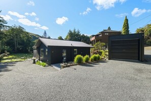 A small, dark-colored building with a gravel driveway and a garage door. - Amalia Cottage - Lake Okareka, Huge Covered Deck, Sleeps 4 (Rotorua)