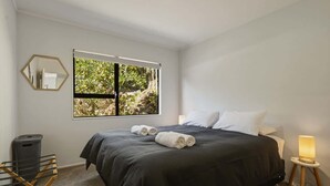 Une chambre avec un grand lit, une fenêtre donnant sur un paysage verdoyant, un miroir et une lampe de chevet.