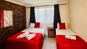 Une chambre d’hôtel avec deux lits, une petite table et une fenêtre avec des rideaux.