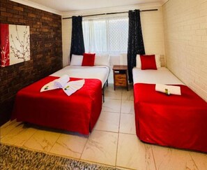 Quarto de hotel com duas camas, uma mesa pequena e uma janela com cortinas.