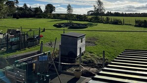 A playground with slides and a small building, surrounded by a grassy field and trees. - Cozy 1 bedroomed apartment in Clackmannanshire (Coalsnaughton)