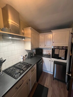 A kitchen with white cabinets, a stainless steel range hood, a dishwasher, and a refrigerator.