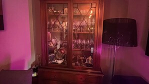 A room with a wooden cabinet containing glassware, a black floor lamp, and a television. - Cozy 1 bedroomed apartment in Clackmannanshire (Coalsnaughton)