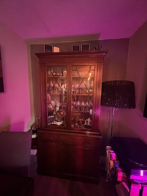 Habitació amb un armari de fusta que conté objectes de vidre i una làmpada de peu negra.