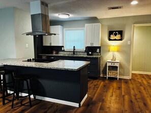 A modern kitchen with a central island, dark cabinetry, and a small side table with a lamp.