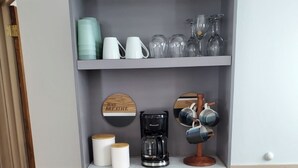 Una kitchenette con cafetera, tarros de almacenamiento y una jarra de café sobre una estantería.