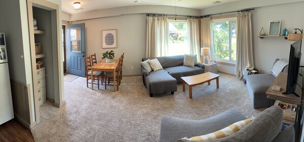 A living room with a sofa, a coffee table, a TV, and a dining area with a table and chairs.