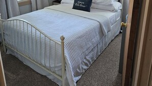Un dormitorio con cama, cortinas, mesita de noche, lámpara y ventana.