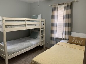 A bunk bed with a ladder, a single bed with a pillow, and a window with curtains.