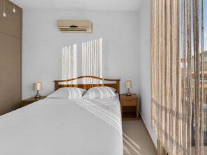 A hotel room with a bed, bedside tables, an air conditioning unit, and a view of the outside. - Villa Amara, Protaras | Private Pool (Protaras)