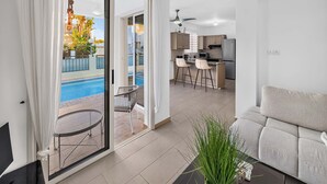 Ein modernes Wohnzimmer mit Sofa, ein Essbereich mit Tisch und Stühlen, eine Küche mit Geräte und eine Glastür, die zum Pool führt.