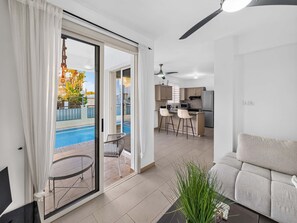Ein modernes Wohnzimmer mit Sofa, ein Essbereich mit Tisch und Stühlen, eine Küche mit Geräte und eine Glastür, die zum Pool führt.