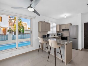 Eine moderne Küche mit integrierter Kochinsel, Barhocker, einem Kühlschrank und einem Deckenventilator.