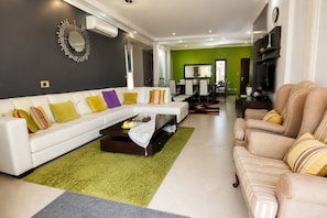 A modern living room with a white sofa, a coffee table, and a green rug. - Luxury Seafront Villa | Private Beach, Pool&Garden (Oroklini)