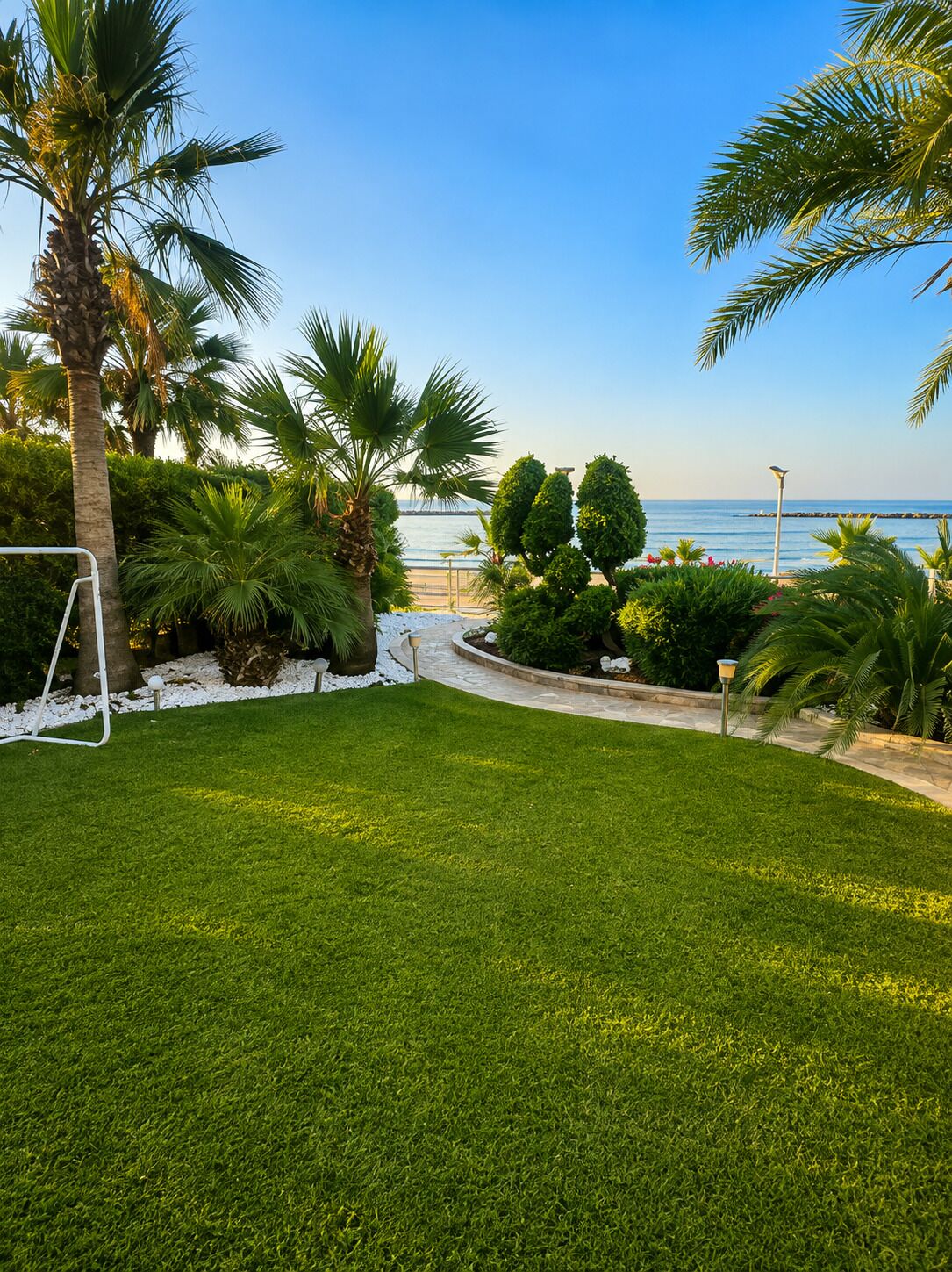 Ein gepflegter Rasen mit einer Palme, einem Fußballtor und Blick auf das Meer.
