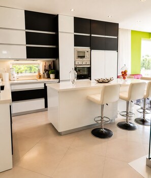 A modern kitchen with a central island, bar stools, and a dining table. - Luxury Seafront Villa | Private Beach, Pool&Garden (Oroklini)