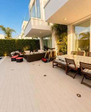 A modern outdoor patio with a dining area, seating, and a treadmill. - Luxury Seafront Villa | Private Beach, Pool&Garden (Oroklini)