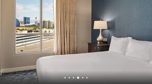 Une chambre d’hôtel avec une grande fenêtre, un lit, une table de chevet avec une lampe et une vue sur le paysage urbain.