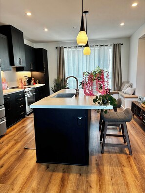 A modern kitchen with a central island, black cabinets, stainless steel appliances, and a wooden floor. - New House W/ Rooftop Near DTLA, Dodgers, Universal, Griffith Park. Great price! (Los Angeles)