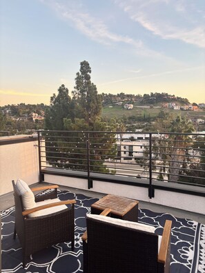 A balcony with wicker furniture, a patterned rug, and a view of a hillside town. - New Bedroom + Rooftop by DTLA, Dodgers, Universal, Griffith Park (Los Angeles)