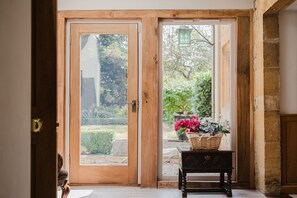 Eine Holztür, die zu einem Garten mit einem Korbtisch und einem Blumenkorb führt.
