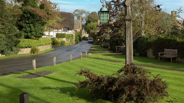 A rural road with a thatched-roof house, a wooden bench, and a street lamp. - The Old Forge - Stanton, Broadway (Stanton, nr Broadway)