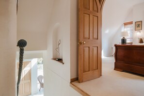 Una puerta de madera con manija de latón, un estante pequeño con un objeto decorativo y un aparador de madera con una lámpara.
