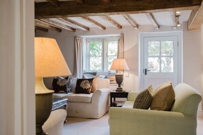 A cozy living room with a sofa, a side table with a lamp, and a window with curtains. - The Old Forge - Stanton, Broadway (Stanton, nr Broadway)