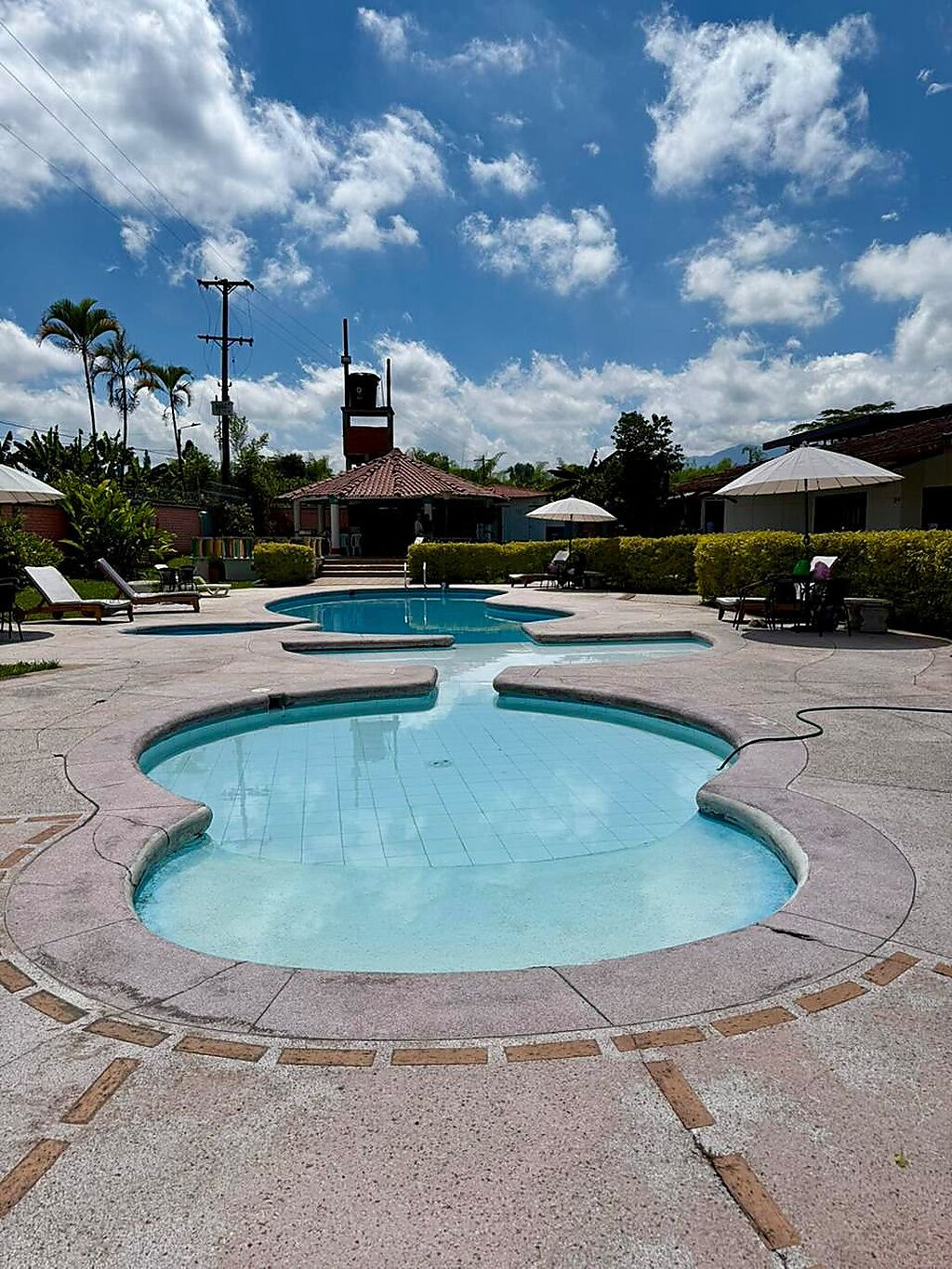A swimming pool area with multiple pools, lounge chairs, and umbrellas.