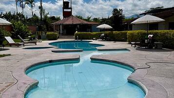 A swimming pool area with multiple pools, lounge chairs, and umbrellas.