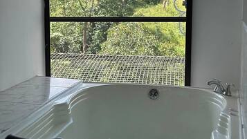 A bathroom with a bathtub, a window with a view of greenery and a road, and a water heater.