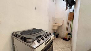 A small kitchen with a gas stove, a sink, and cleaning tools. - Cozy house in Itagua (Ubatuba)