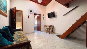 A room with a bed, a table with chairs, a TV mounted on the wall, and a staircase. - Cozy house in Itagua (Ubatuba)