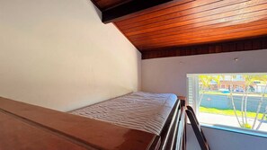 Quarto com teto de madeira, janela com vista para o exterior e cama com colcha estampada.
