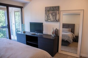 Ein Schlafzimmer mit einem Bett, einem Fernseher auf einer Kommode, einem Spiegel und einem Fenster.