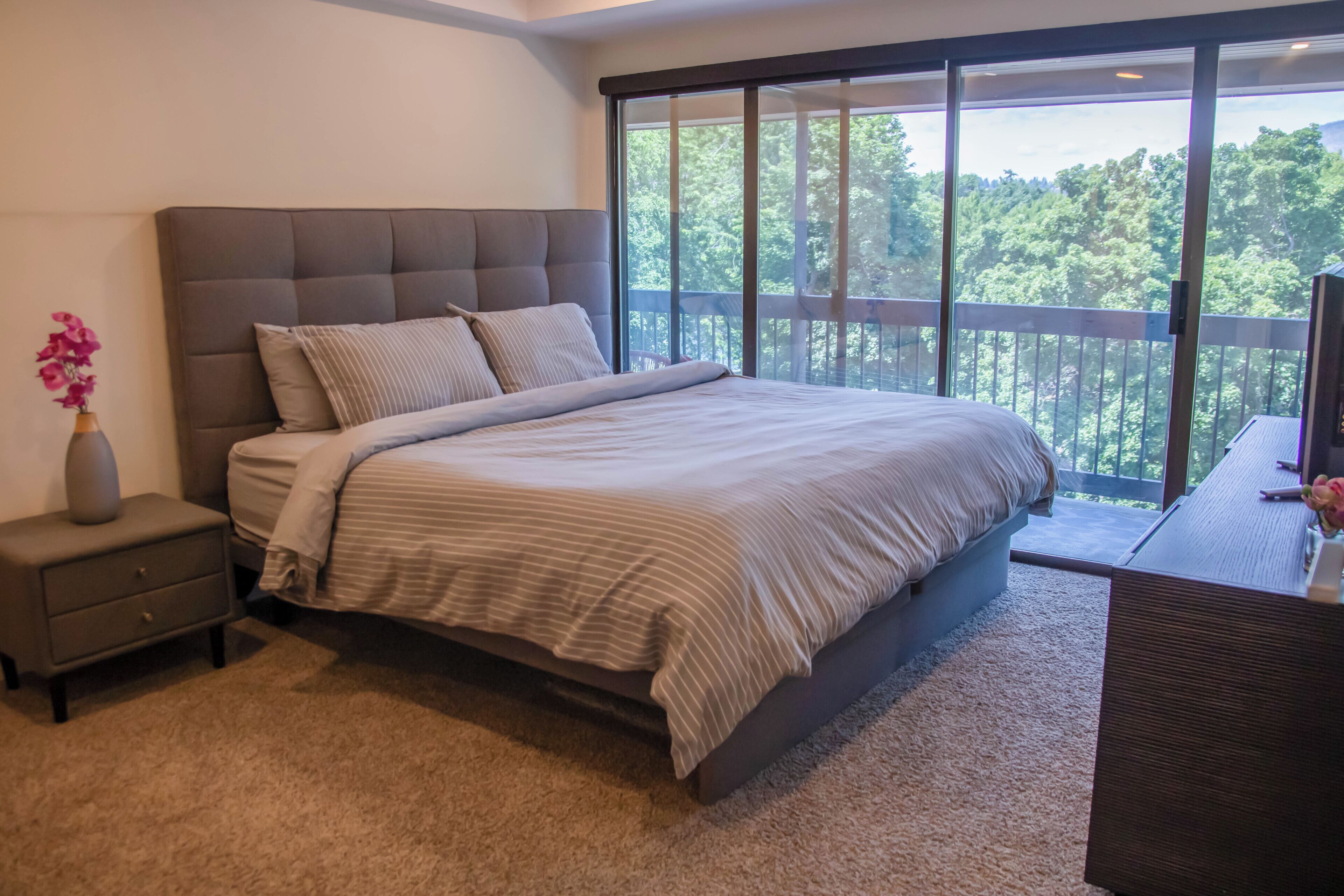 Une chambre à coucher avec un grand lit, une table de chevet, une commode et une vue sur l’extérieur grâce à un balcon.