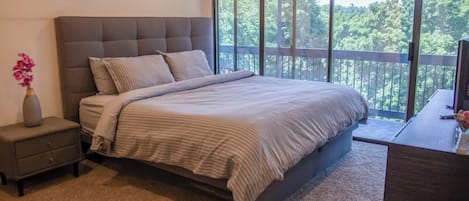 Une chambre à coucher avec un grand lit, une table de chevet, une commode et une vue sur l’extérieur grâce à un balcon.